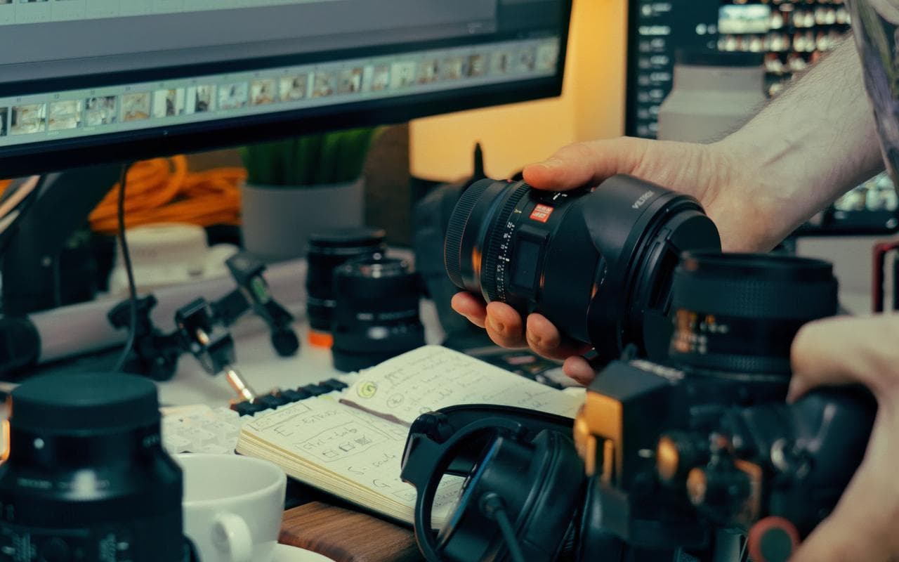 Editing suite with a timeline on screen, lenses and a notebook on the desk